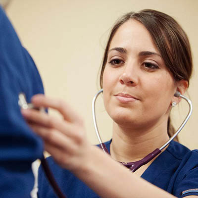 A nurse listens to someone's heart beat through a stethoscope.